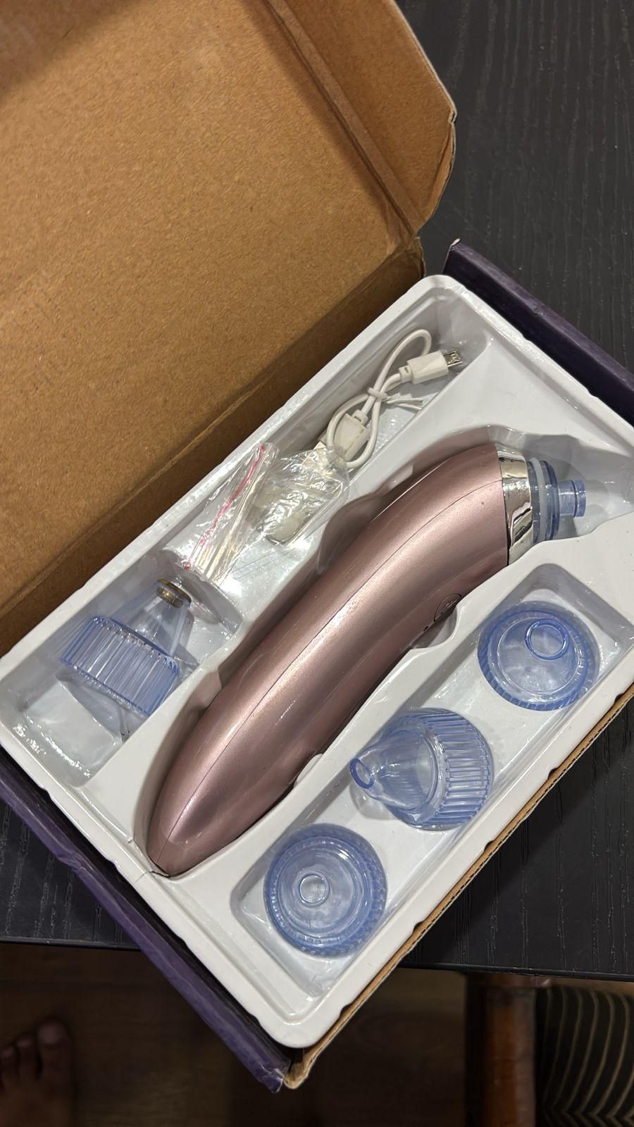 Vacuum acne pore cleaner in rose gold with multiple attachments and USB charging cable in an open box