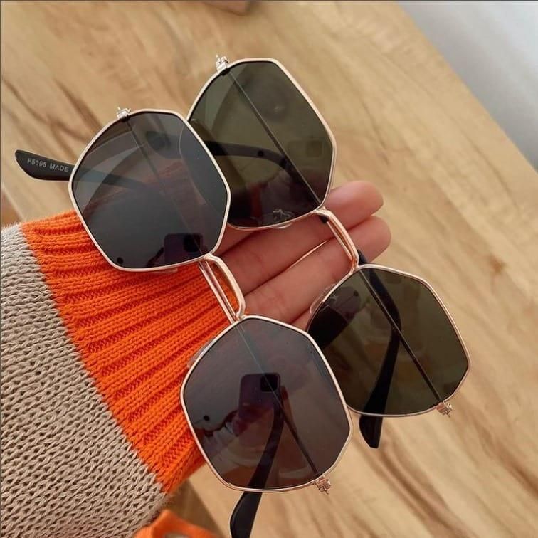 Stylish unique octagon sunglasses in a hand with a trendy sweater background